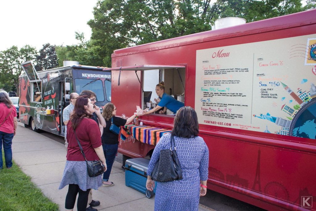People ordering food from food trucks outside a beer tasting event.