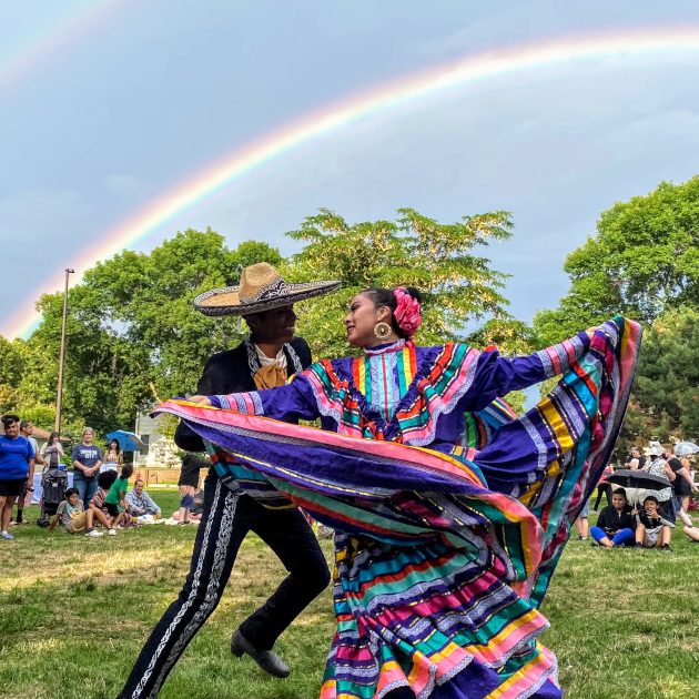 Mexican ballet folklorico performers dancing beneath a rainbow at the 2022 Monarch Festival in Columbia Heights, Minnesota.