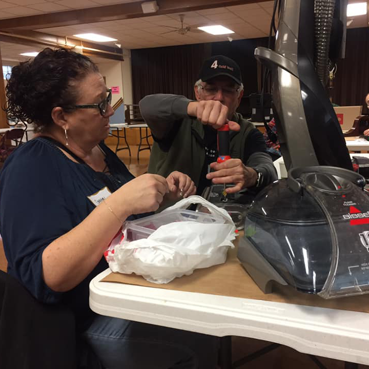 A skilled volunteer helps a resident fix their vacuum cleaner at a fix-it clinic.