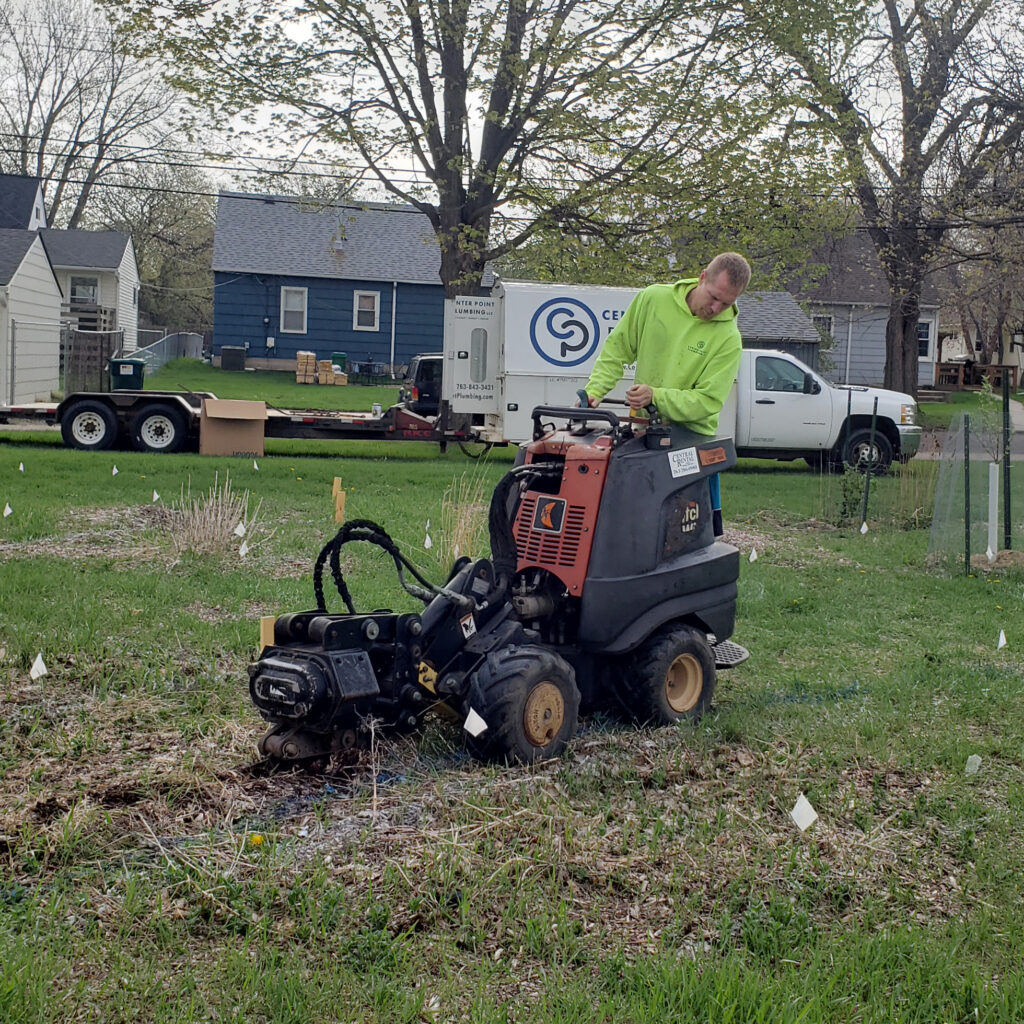 A plumber uses a machine to pull new water lines underground into the garden.